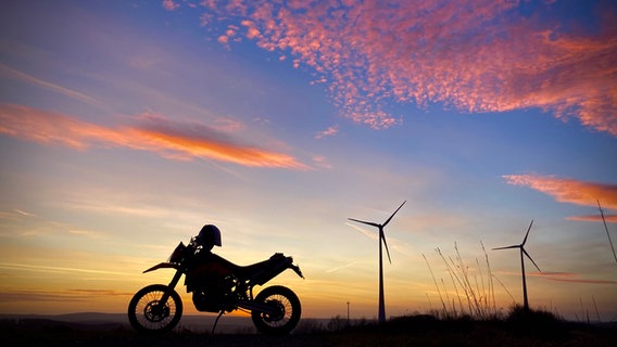 Vor einem Sonnenuntergang zeichnet sich ein Motorrad ab. © NDR Foto: Frank May