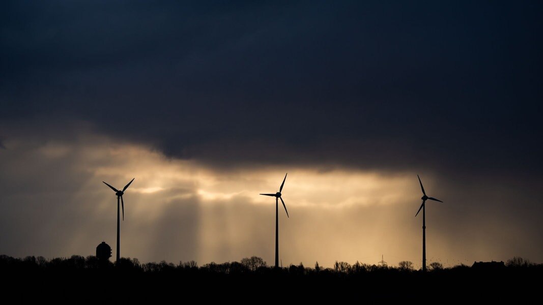 Mehrere Windräder stehen auf einem Feld in Niedersachsen, dunkle Wolken ziehen vorbei.