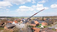 Ein Windradflügel wird auf einem Schwertransport durch ein Dorf gefahren. © NDR 