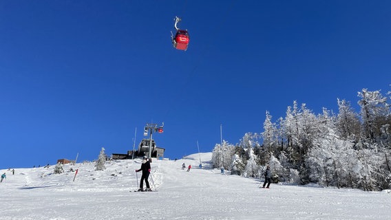 Skifahrende auf dem Sonnenhang Wurmberg. Oben: eine rote Gondel der Wurmbergseilbahn. © NDR Foto: Jan Fragel