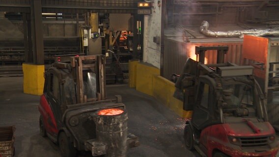 Arbeiter fahren flüssiges Eisen mit Gabelstaplern in einer Fabrik umher. © NDR 