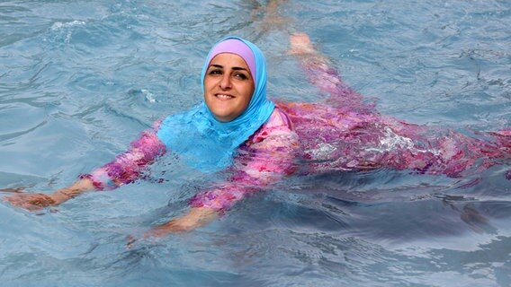 Ein Mädchen sitzt in einen Burkini gekleidet am Rand eines Schwimmbeckens. © dpa Foto: Stephanie Pilick