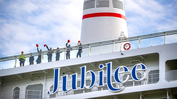 Die Besatzung winkt vom neuen Kreuzfahrtschiff der Papenburger Meyer Werft "Carnival Jubilee", das über die Ems zur Nordsee überführt wird. © dpa-Bildfunk Foto: Sina Schuldt