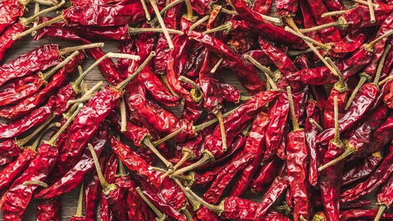 Viele rote Chilis liegen auf einem Tisch. © picture alliance/Zoonar Foto: Jiri HERA