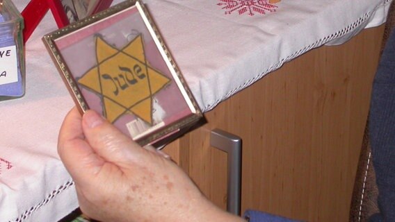 Albrecht Weinberg hält einen Bilderrahmen in der Hand. Darin ist sein Judenstern zu sehen. © NDR Foto: Birgit Schütte