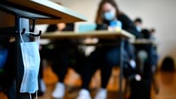 Eine Mund-Nasen-Maske hängt an einem Tisch im Klassenzimmer. Eine Mund-Nasen-Maske hängt an einem Tisch im Klassenzimmer. © picture alliance/Eibner-Pressefoto/Weber/Eibner-Pressefoto Foto: Weber/Eibner-Pressefoto