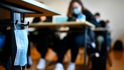 Eine Mund-Nasen-Maske hängt an einem Tisch im Klassenzimmer. © picture alliance/Eibner-Pressefoto/Weber/Eibner-Pressefoto Foto: Weber/Eibner-Pressefoto