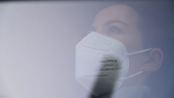 Eine Frau mit FFP2-Maske schaut aus einem Fenster. © picture alliance/Frank May Foto: Frank May