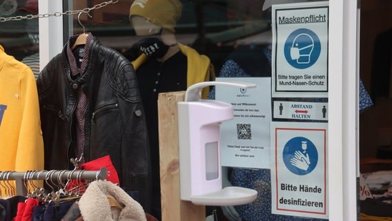 Schilder neben der Eingangstür eines Bekleidungsgeschäftes weisen darauf hin, dass im Laden Maskenpflicht besteht und die Hände desinfiziert werden müssen. © dpa-Bildfunk Foto: Peter Kuchenbuch-Hanken
