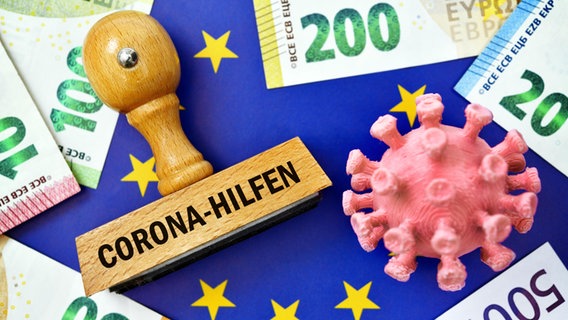 Ein Stempel mit der Aufschrift: "Corona-Hilfen" neben einem Stilisierten Virus und Geldscheinen. © picture alliance Foto: Bildagentur-online/Ohde
