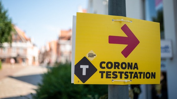 Ein gelbes Schild mit pinkem Pfeil weist den Weg zu einem Corona-Testzentrum. © picture alliance/dpa Foto: Philipp Schulze