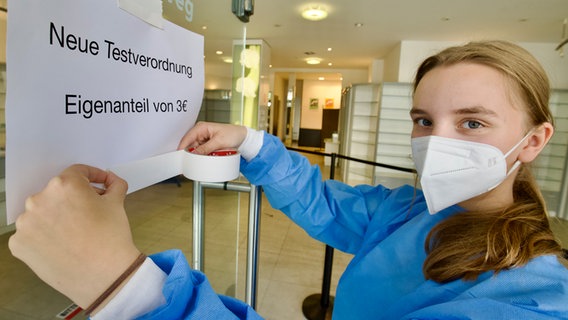Eine Frau klebt ein Schild mit dem Text "Neue Testverordnung - Eigenanteil von drei Euro" an eine Glaswand. © picture alliance Foto: Andreas Dunker