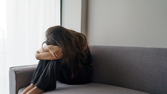 Eine Frau sitzt zusammengekauert auf einem Sofa. © picture alliance/Zoonar/Sirijit Jongcharoenkulchai Foto: Sirijit Jongcharoenkulchai