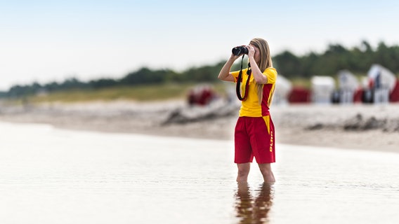 Eine Frau von der DLRG steht mit einem Feldstecher am Meer. © DLRG 