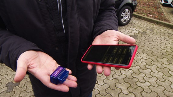 A man holds a smartphone and a battery tester in his hands.  © NDR 