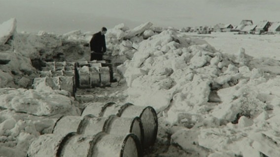 Ein Mann steht mit einigen Fässern im Schnee.  