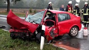 Einsatzkräfte der Feuerwehrt stehen an einem Unfallort neben einem stark zerstörten Auto. © TeleNewsNetwork 