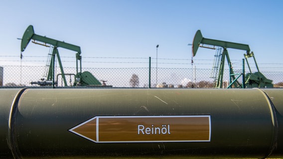 Tiefpumpen für die Erdölförderung stehen hinter einer Leitung für Roherdöl in Emlichheim. © dpa-Bildfunk Foto: Lino Mirgeler/dpa