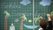 Eine Lehrerin schreibt "Schöne Sommerferien" an die Tafel © picture alliance/dpa Foto: Ina Fassbender