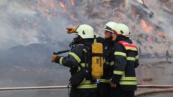 Drei Einsatzkräfte der Feuerwehr stehen vor einem brennenden Komposthaufen. © NDR Foto: Stefan Rampfel