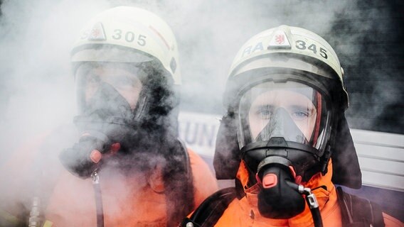 Zwei Feuerwehrleute mit Atemschutzmasken sind von Rauch umhüllt. © NDR Foto: Julius Matuschik