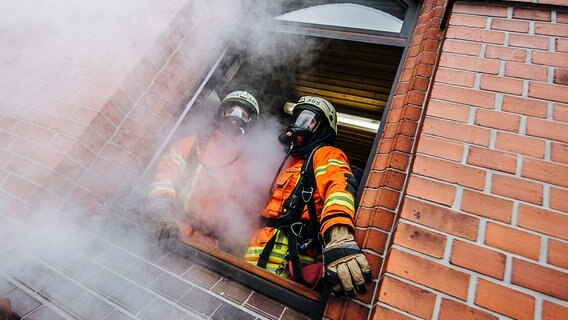 Zwei Feuerwehrleute stehen am Fenster eines Hauses, aus dem Rauch herausdringt. © NDR Foto: Julius Matuschik