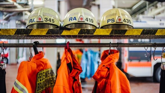 Feuerwehrjacken hängen an einer Stange, auf einer Ablage darüber liegen Helme. © NDR Foto: Julius Matuschik
