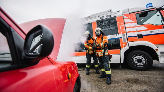 Zwei Feuerwehrleute löschen ein brennendes Auto. © NDR Foto: Julius Matuschik