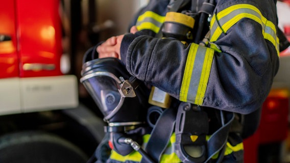 Ein Feuerwehrmann steht mit Atemschutzmaske vor einem Feuerwehrauto. © imago images Foto: Cavan Images