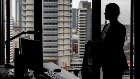 Eine Frau steht an ihrem Arbeitsplatz in einem Hochhaus am Fenster. © Hannes P. Albert/dpa Foto: Hannes P. Albert/dpa