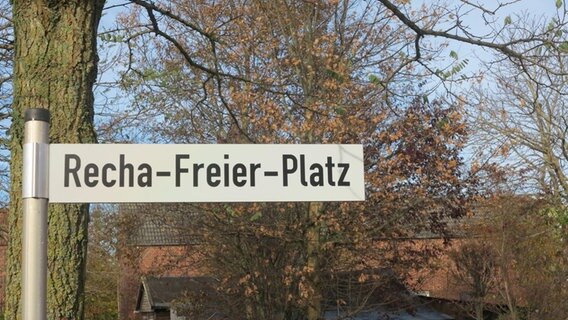 Auf einem Straßenschild steht "Recha-Freier-Platz", im Hintergrund sind Bäume ohne Blätter und ein Haus zu sehen. © Kaja Schierl Foto: Kaja Schierl