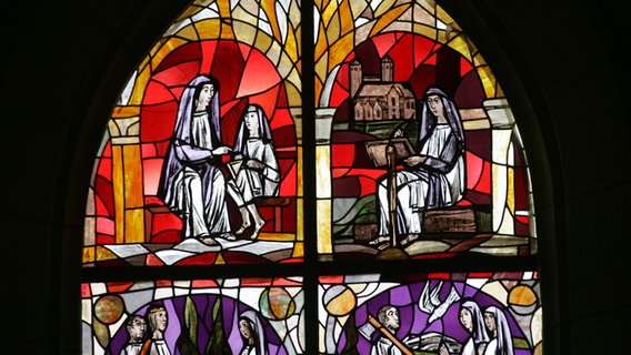 Auf einem Kirchen-Fenster aus buntem Glas sind mehrere Frauen-Figuren dargestellt. © Stadt Bad Gandersheim 