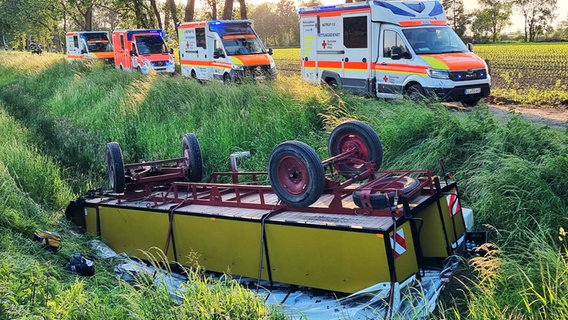 Ein Planwagen liegt umgekippt in einem Graben im Landkreis Freren. Dahinter stehen vier Krankenwagen. © Nord-West-Media TV 
