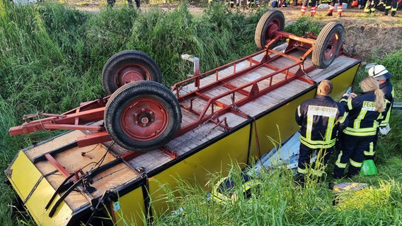 Ein Planwagen liegt umgekippt in einem Graben im Landkreis Freren. Daneben Feuerwehr. © NWM-TV/dpa 