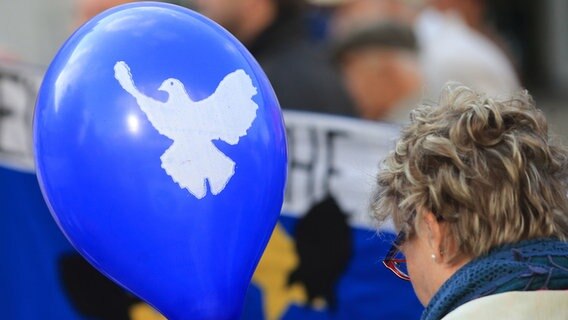 Ein blauer Luftballon mit dem Symbol einer weißen Friedenstaube wird während einer Kundgebung getragen. © dpa-Bildfunk Foto: Jens Wolf