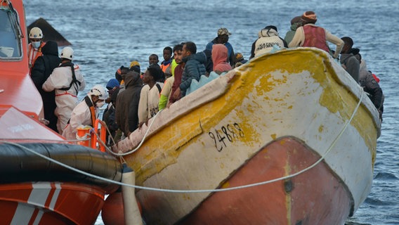 Auf dem Bild zu sehen ist ein Boot mit geflüchteten Menschen auf hoher See. Ein Rettungsboot hat gerade längsseits festgemacht. © picture alliance/dpa/EUROPA PRESS | Europa Press Foto: picture alliance/dpa/EUROPA PRESS | Europa Press