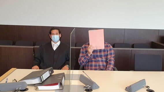 Rechtsanwalt Nicolai Mameghani sitzt im Prozess wegen Geiselnahme neben dem Angeklagten, der sich einen Aktendeckel vor das Gesicht hält. © dpa-Bildfunk Foto: Martin Höke