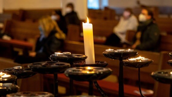 Gäste des ökumenischen Gedenkgottesdienstes sitzen in der Kirche. Im Vordergrund ist eine Kerze. © picture alliance/dpa | Axel Heimken Foto: Axel Heimken