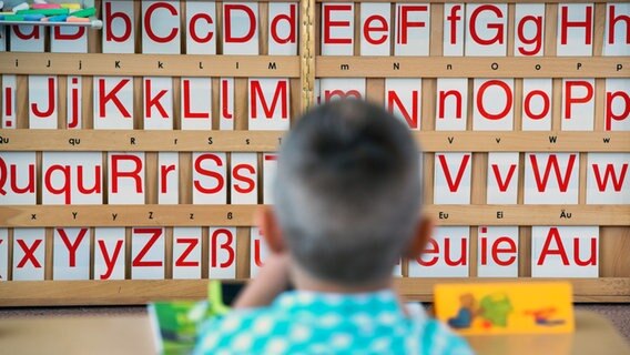 Ein Kind sitzt an einem Tisch; im Hintergrund sind Buchstaben zu sehen. © picture alliance/dpa Foto: Arno Burgi
