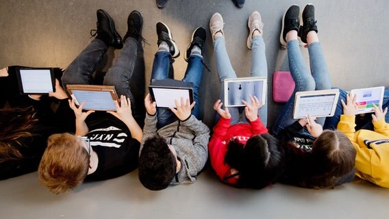 Schüler eines Gymnasiums sitzen in einer Reihe auf dem Boden und lernen mit einem Tablet. © dpa-Bildfunk Foto: Julian Stratenschulte