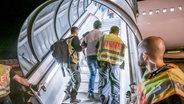 Polizeibeamte begleiten einen Mann im Zuge eines Abschiebungsverfahrens über die Gangway in ein Flugzeug. © picture alliance/dpa-Bildfunk Foto: Michael Kappeler