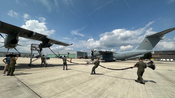 Bundeswehr Soldaten ziehen einen Schlauch zur Luftbetankung aus einem Flugzeug. © NDR Foto: Bertil Starke