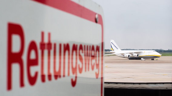 Ein Transportflugzeug vom Typ Antonov 124-100 steht auf dem Rollfeld des Flughafens - fotografiert mit einem Schild mit Aufschrift "Rettungsweg". © dpa-Bildfunk Foto: Julian Stratenschulte