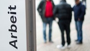 Männer stehen vor der Bundesagentur für Arbeit in Hannover. Im Vordergrund ein Schriftzug "Arbeit". © picture alliance Foto: Julian Stratenschulte