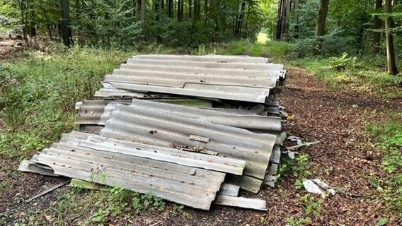 An einem Waldweg sind mehrere gewellte Asbestplatten übereinandergestapelt. © Polizei Nienburg 