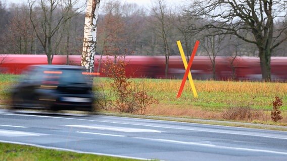 Ein Protest-Kreuz steht auf einem Feld nahe der geplanten Neubaustrecke und einer bestehenden Trasse. © dpa-Bildfunk Foto:  Jonas Walzberg/dpa