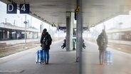 Eine Frau wartet mit einem Koffer am Gleis 4 im Hauptbahnhof Hannover und spiegelt sich in einer Glasscheibe. © dpa bildfunk Foto: Julian Stratenschulte