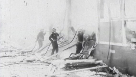 Drei Einsatzkräfte der Feuerwehr löschen einen brennenden Güterwaggon auf einer historischen Schwarz-Weiß-Aufnahme © NDR 