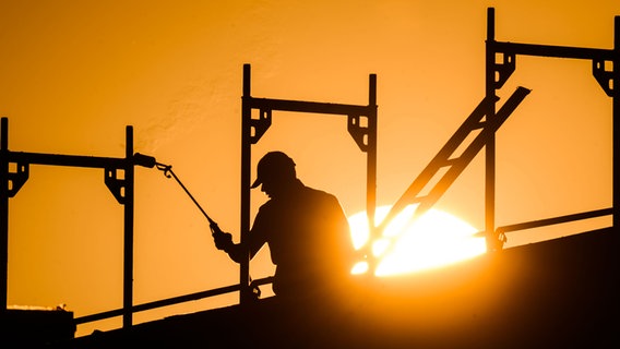 Ein Bauarbeiter steht mit einem Gasbrenner beim Bau eines Mehrfamilienhauses auf einem Gerüst. © picture alliance/dpa Foto: Julian Stratenschulte