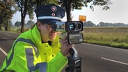 Eine Polizistin hinter einem Blitzer vor einer Landstraße. © NDR Foto: Claudia Wohlsperger